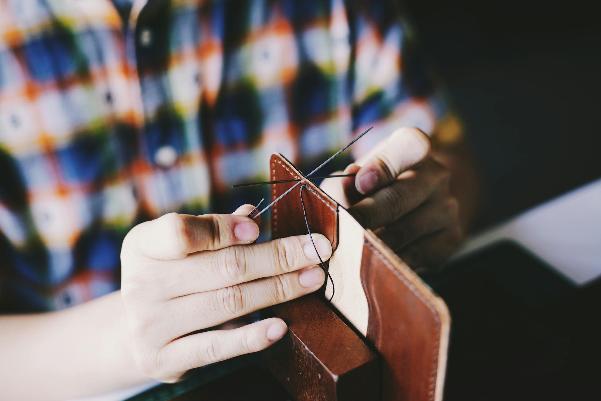 Close-up of a person hand-stitching leather, showcasing detailed craftsmanship and DIY skills.